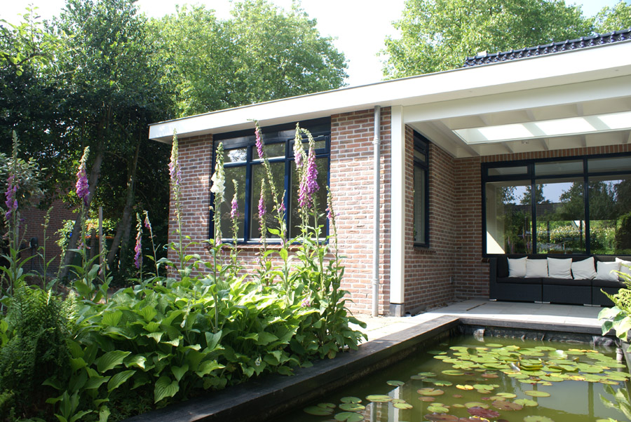 Achterkant van een pas geschilderd gemoderniseerde bungalow met vijver, overdekt terras en bloeiende vingerhoedskruid
