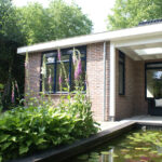 Achterkant van een pas geschilderd gemoderniseerde bungalow met vijver, overdekt terras en bloeiende vingerhoedskruid